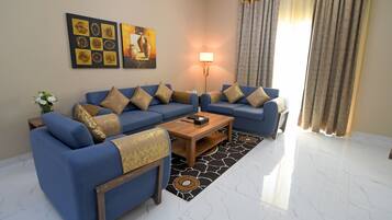 A living room with a blue sofa set, a wooden coffee table, a floor lamp, and a patterned rug.