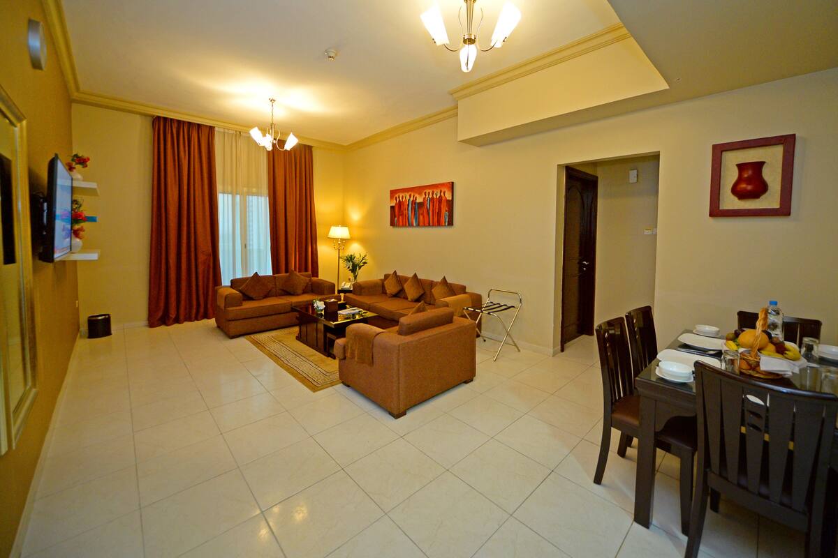 A living room with a sofa set, a dining table with chairs, a lamp, and a painting on the wall.