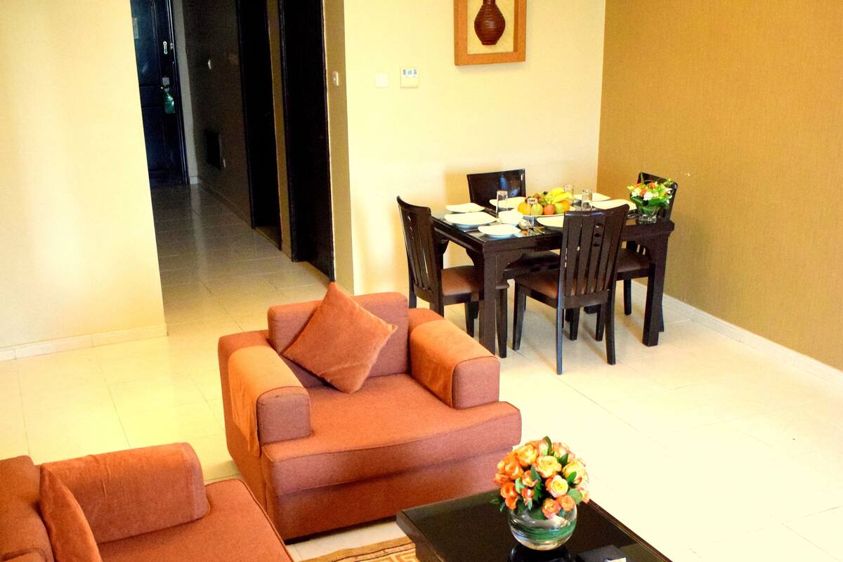 A living room with a sofa set, a coffee table with a vase, and a dining area with chairs and a table.