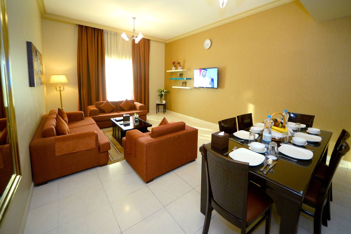 A hotel room with a living area, dining table set for four, and a TV mounted on the wall.