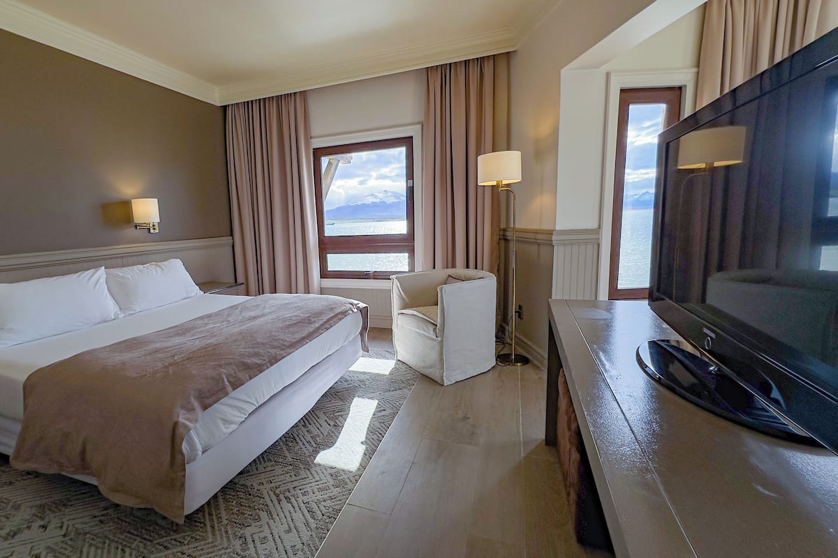 A hotel room with a large bed, a desk with a television, a chair, and a window with curtains.