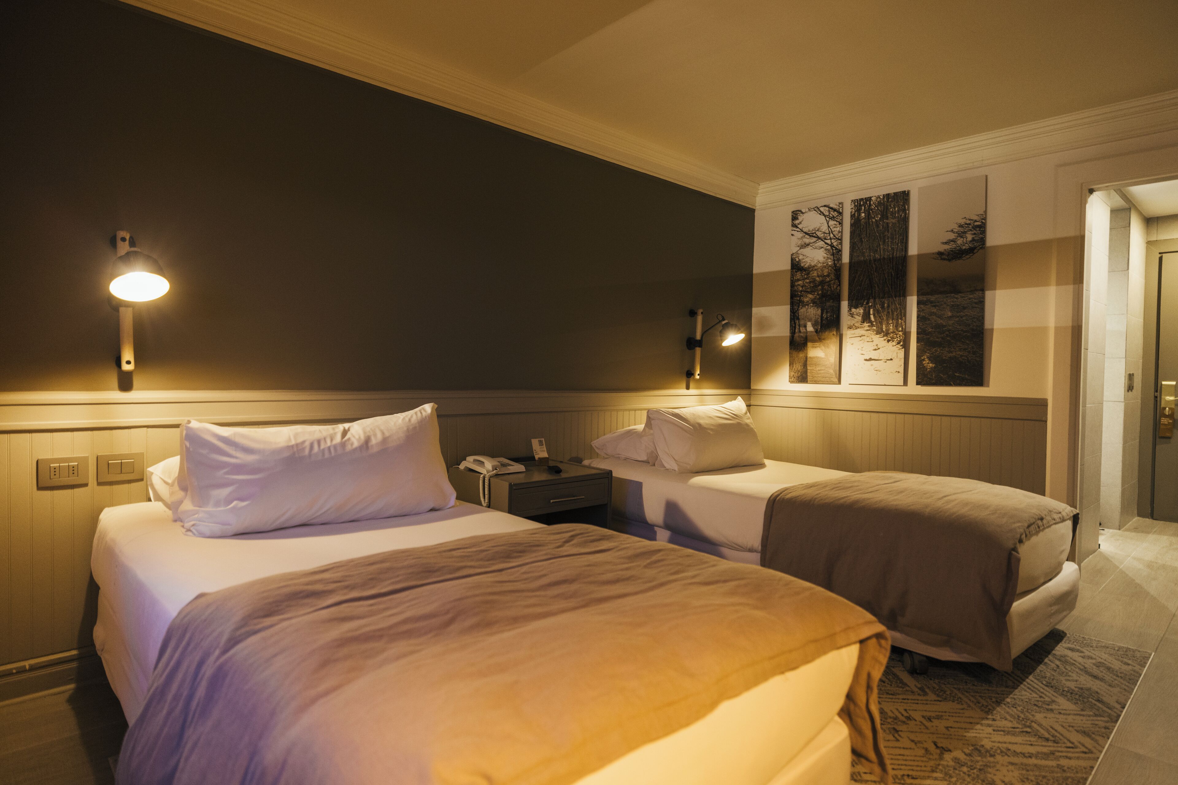 Une chambre d’hôtel avec deux lits, une table de chevet et une lampe fixée au mur.