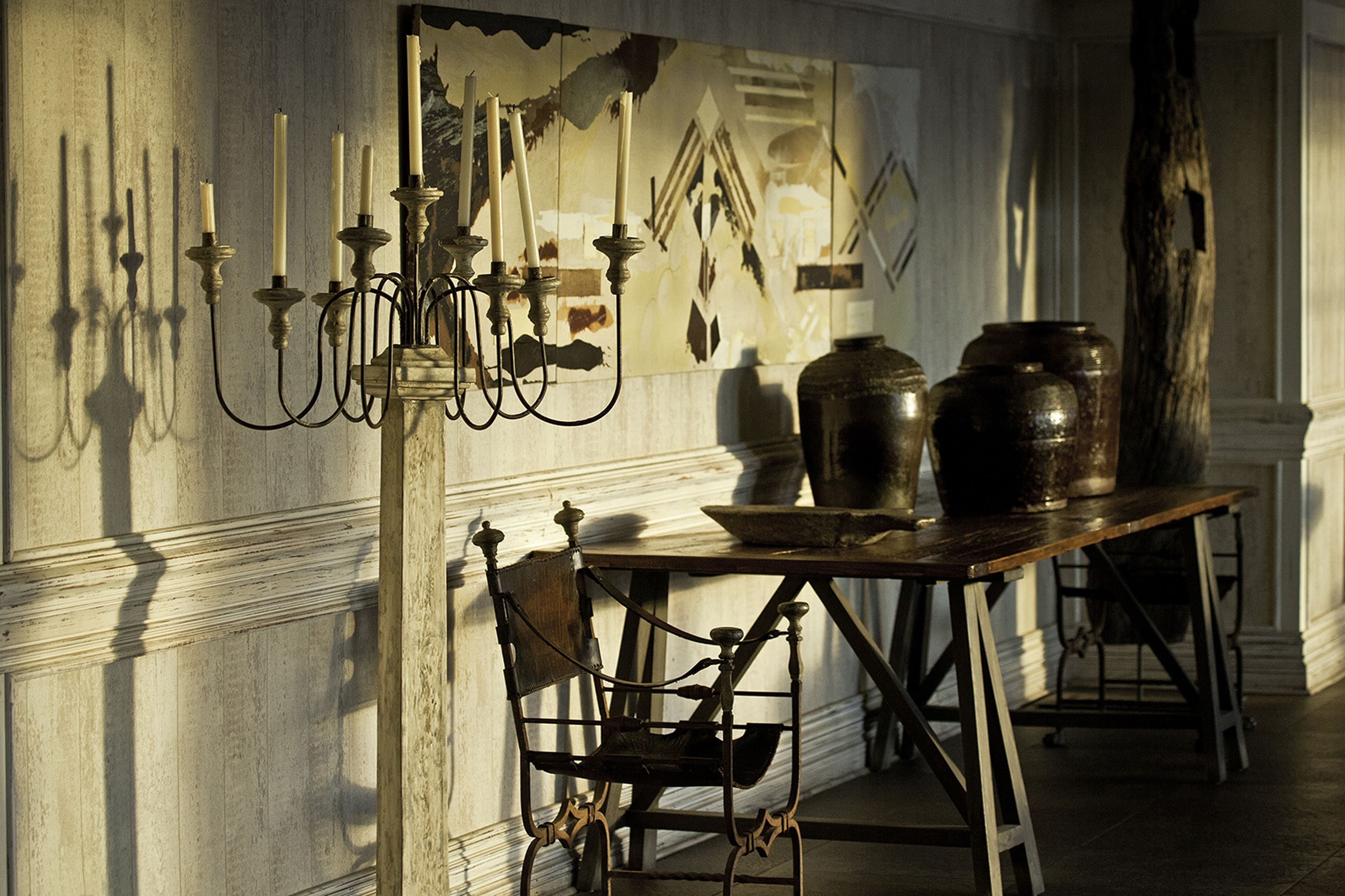 A room with a table, chairs, and a candelabra with candles. There are large vases on the table and a painting on the wall.