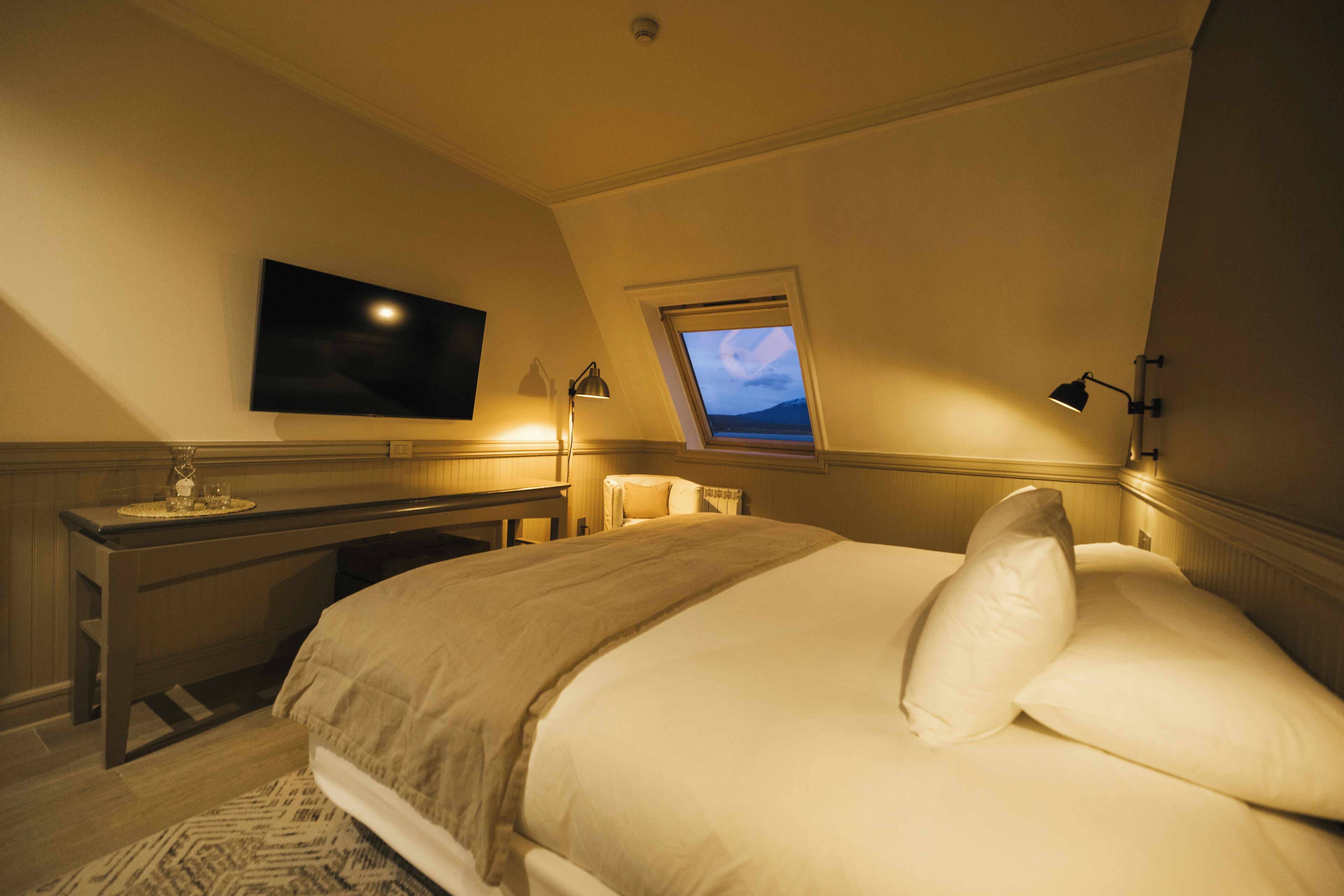 Une chambre à coucher avec un lit, un téléviseur fixé au mur, un bureau et une fenêtre donnant sur un beau paysage.