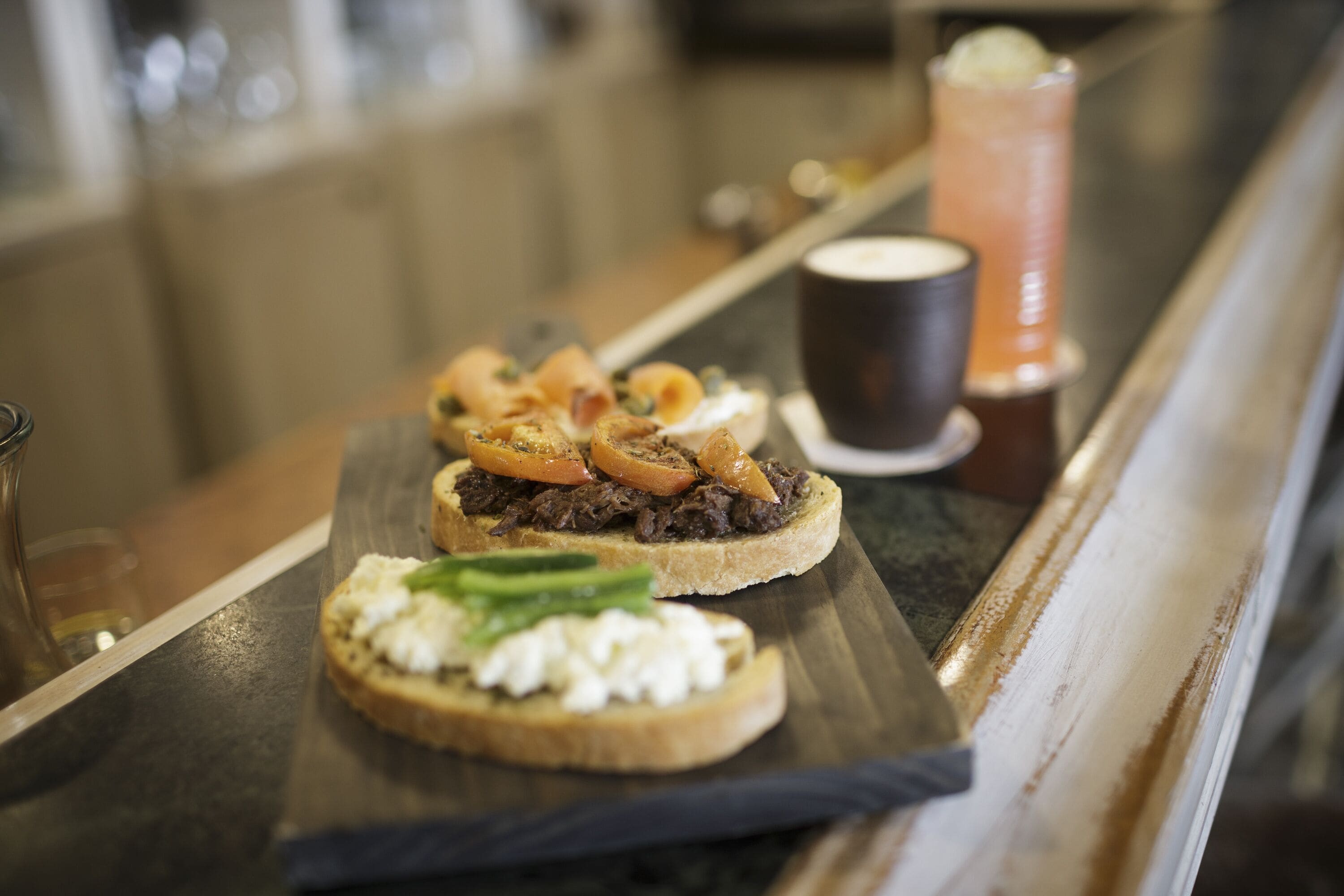 Una barra con dos tostadas cubiertas de carne y verduras, una taza de café y un vaso de té helado.