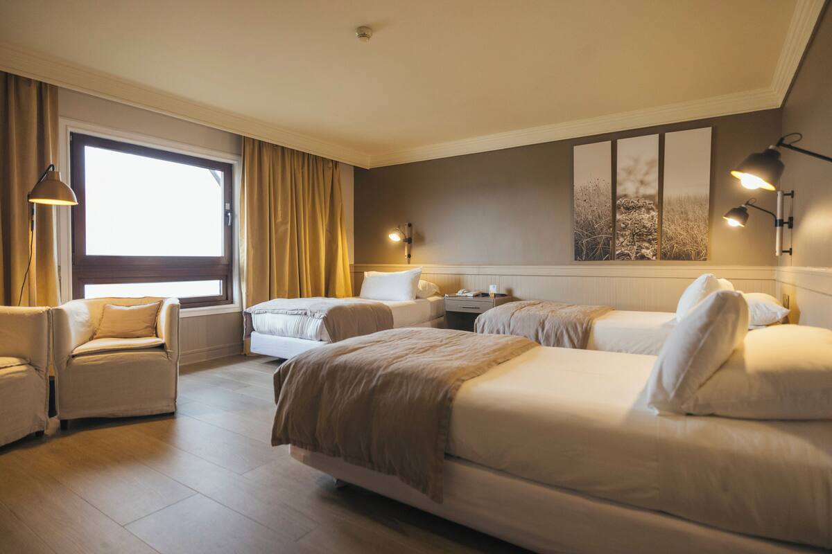 A hotel room with two beds, a sofa, a desk, and a large window with curtains.