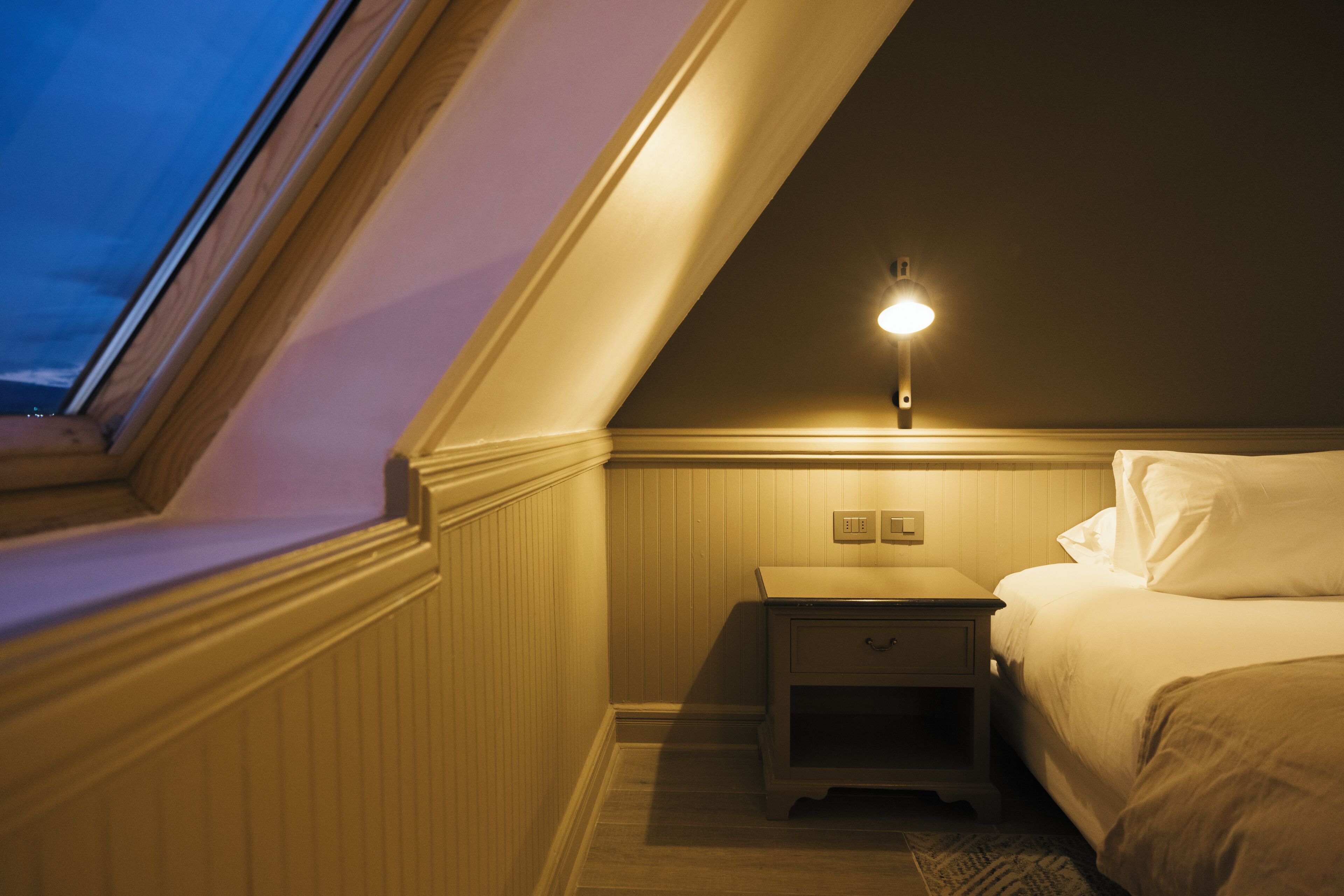 Un dormitorio con techo inclinado, una mesita de noche, una lámpara y una cama.