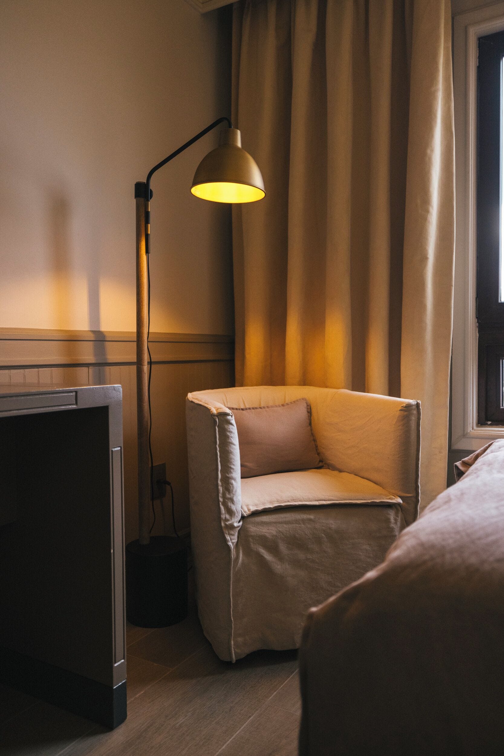 A hotel room with a bed, a chair, a desk, and a lamp.