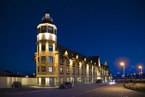 A hotel with a prominent tower, multiple windows, and a paved street with cars parked in front. - Hotel Costaustralis (Natales)