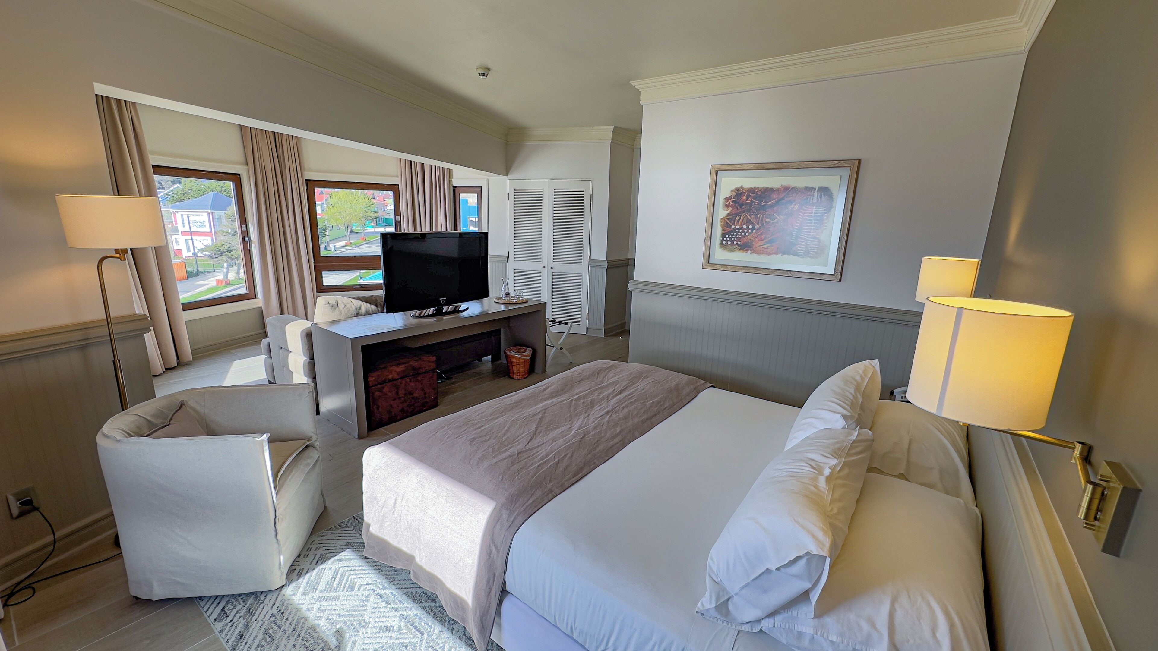 Une chambre d’hôtel avec un lit, un bureau avec une télévision, une chaise et une fenêtre avec des rideaux.