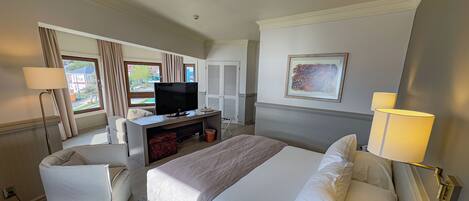 Une chambre d’hôtel avec un lit, un bureau avec une télévision, une chaise et une fenêtre avec des rideaux.