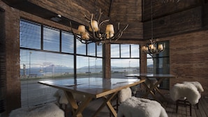 A rustic interior with a large wooden table, fur-covered stools, and a chandelier with antlers. - Hotel Costaustralis (Natales)