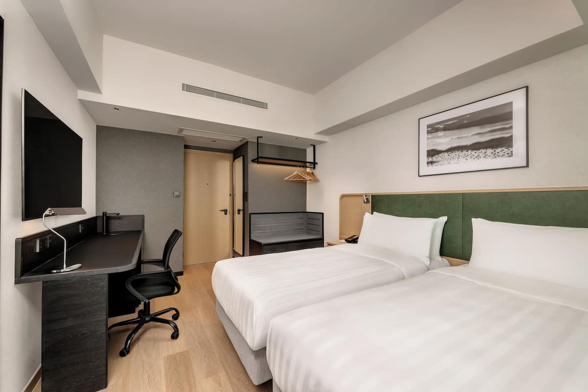 A hotel room with a bed, a desk, a chair, a TV, and a painting on the wall.