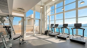 Un gimnasio con cintas de correr, máquinas de pesas y grandes ventanales con vistas al agua.