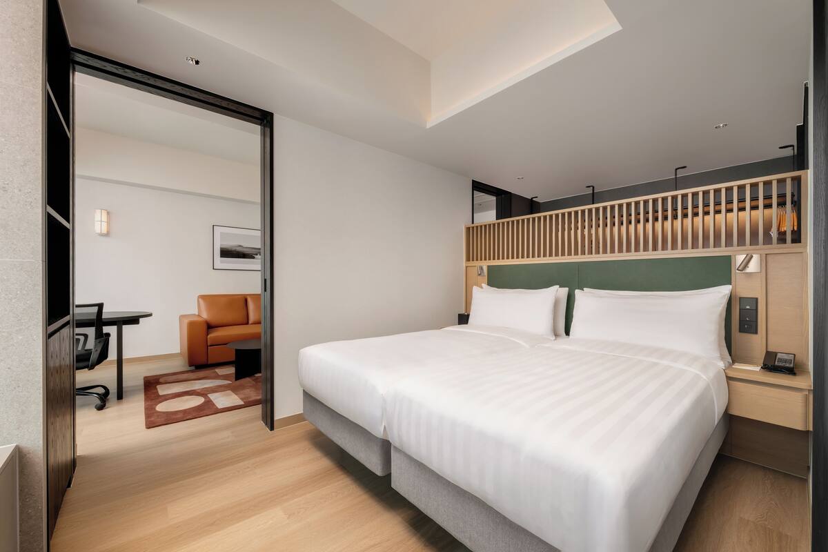A modern hotel room with a large bed, a desk, a chair, and a view of the city.