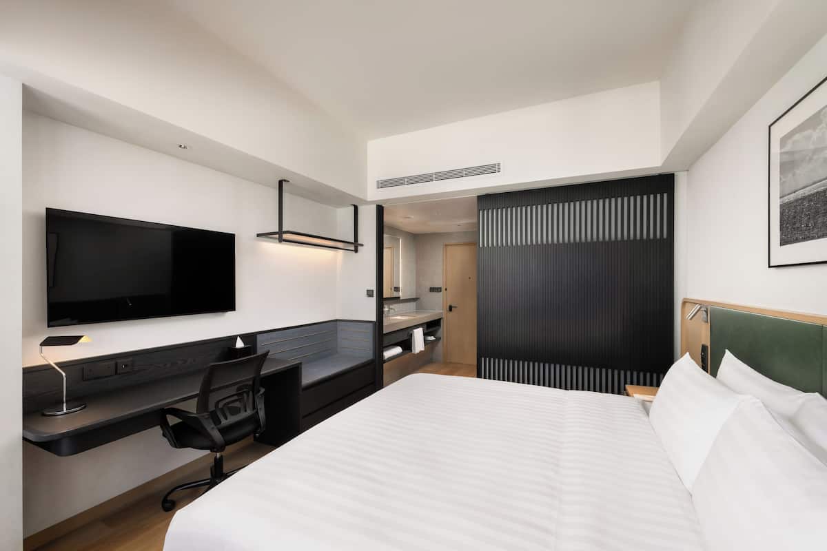 A hotel room with a bed, desk, chair, TV, and a bathroom.