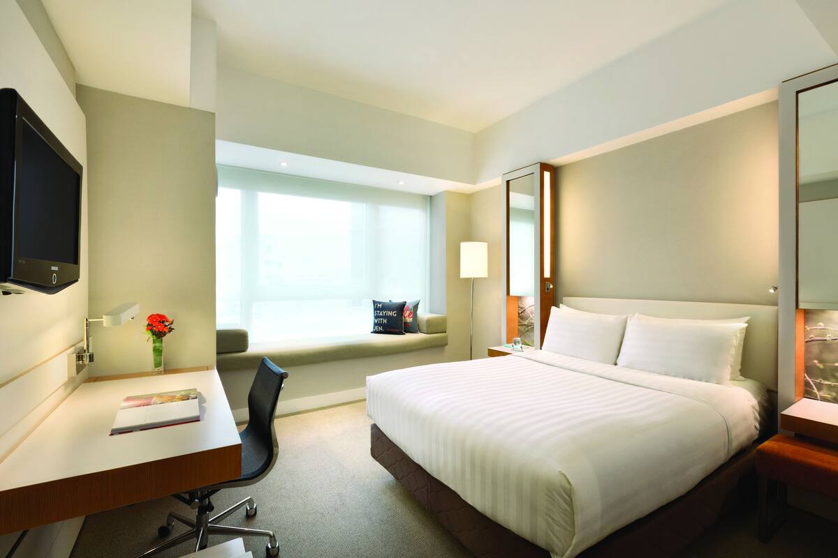 A hotel room with a large bed, a desk with a chair, a TV, and a window with a view.