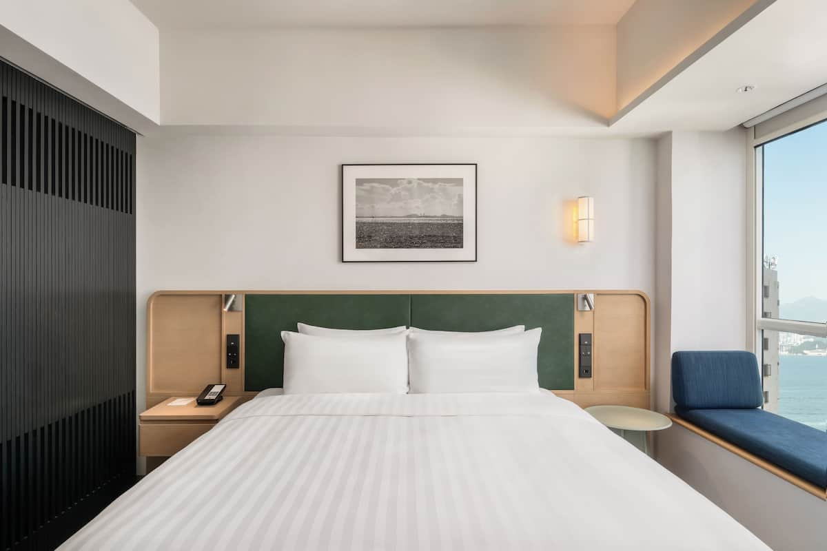 A hotel room with a bed, bedside tables, a phone, a picture on the wall, and a window with a view.