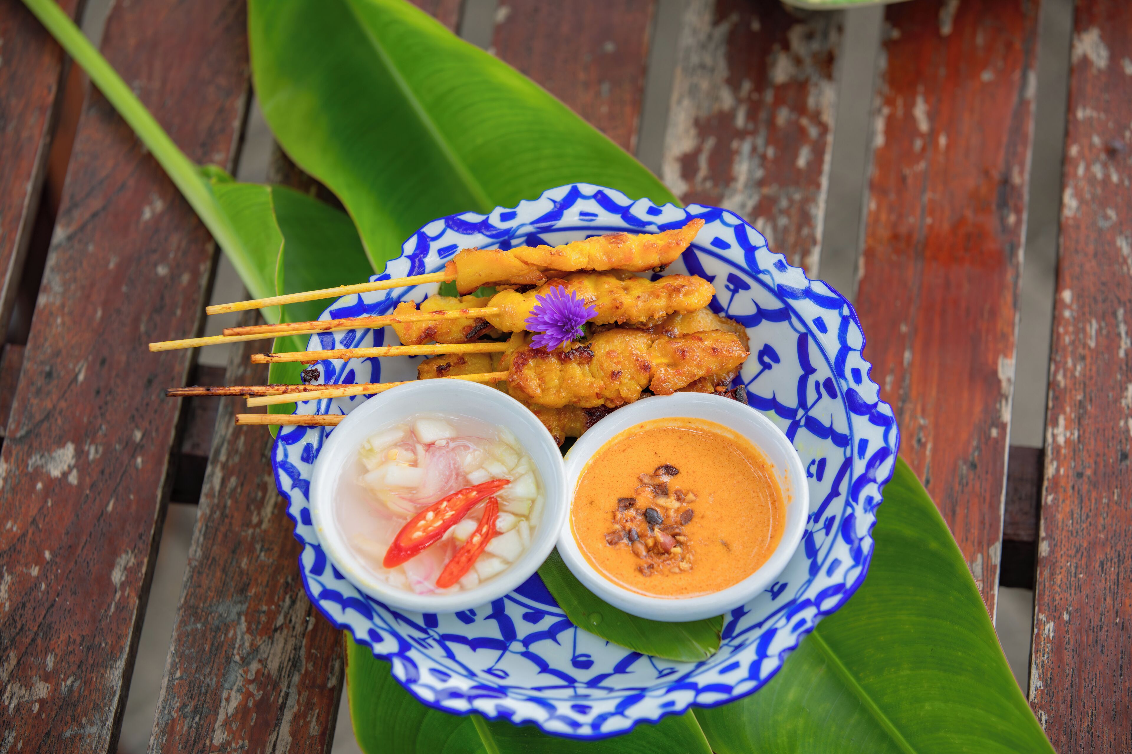 Une assiette de brochettes de satay, accompagnée de deux sauces pour tremper et d’un petit bol de piment.