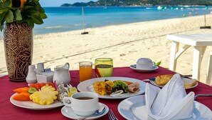 Ein Frühstück am Strand mit Tisch, Speisen, Getränken und einer dekorativen Vase.