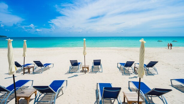 Ein Strand mit Reihen von Liegestühlen und Sonnenschirmen, einem klaren blauen Himmel und ruhigem türkisblauem Wasser.