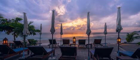 A beachside seating area with lounge chairs and umbrellas, overlooking the ocean.