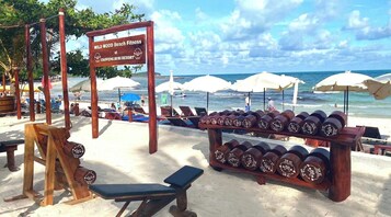 Zona de ejercicios junto a la playa con equipamiento y un cartel que indica Wild Wood Beach Fitness en el Resort Chaweng Buri.