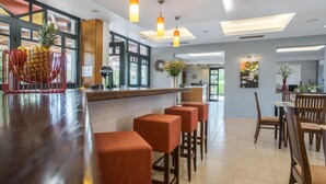 Un área de bar moderna con mostrador de madera, taburetes naranjas e iluminación colgante.
