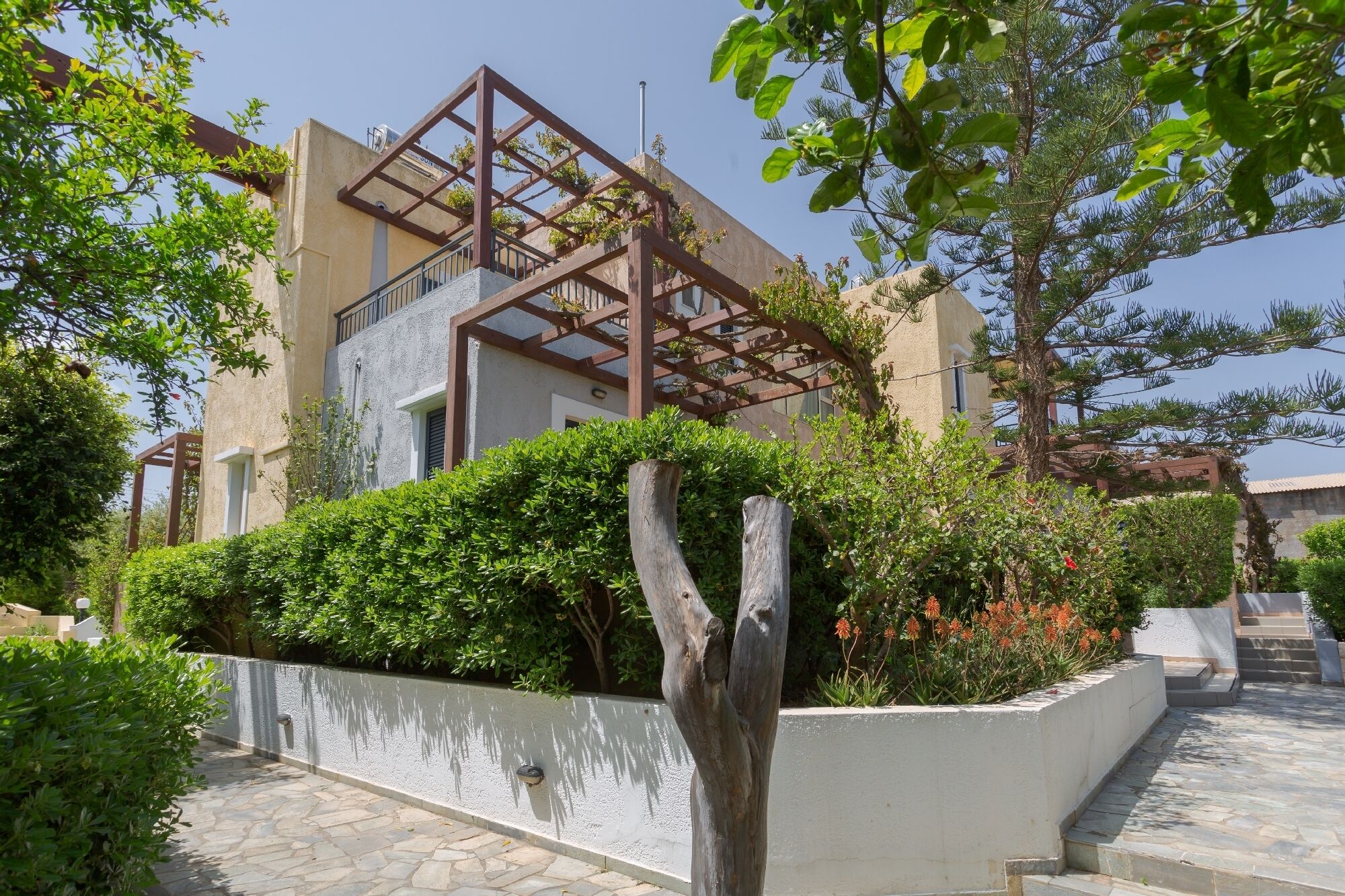 Un edificio moderno con fachada de piedra, una pérgola de madera y un camino de piedra.