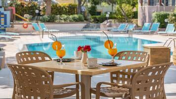 Un espace repas aménagé au bord de la piscine, avec deux tables, des chaises et une vue sur la piscine.