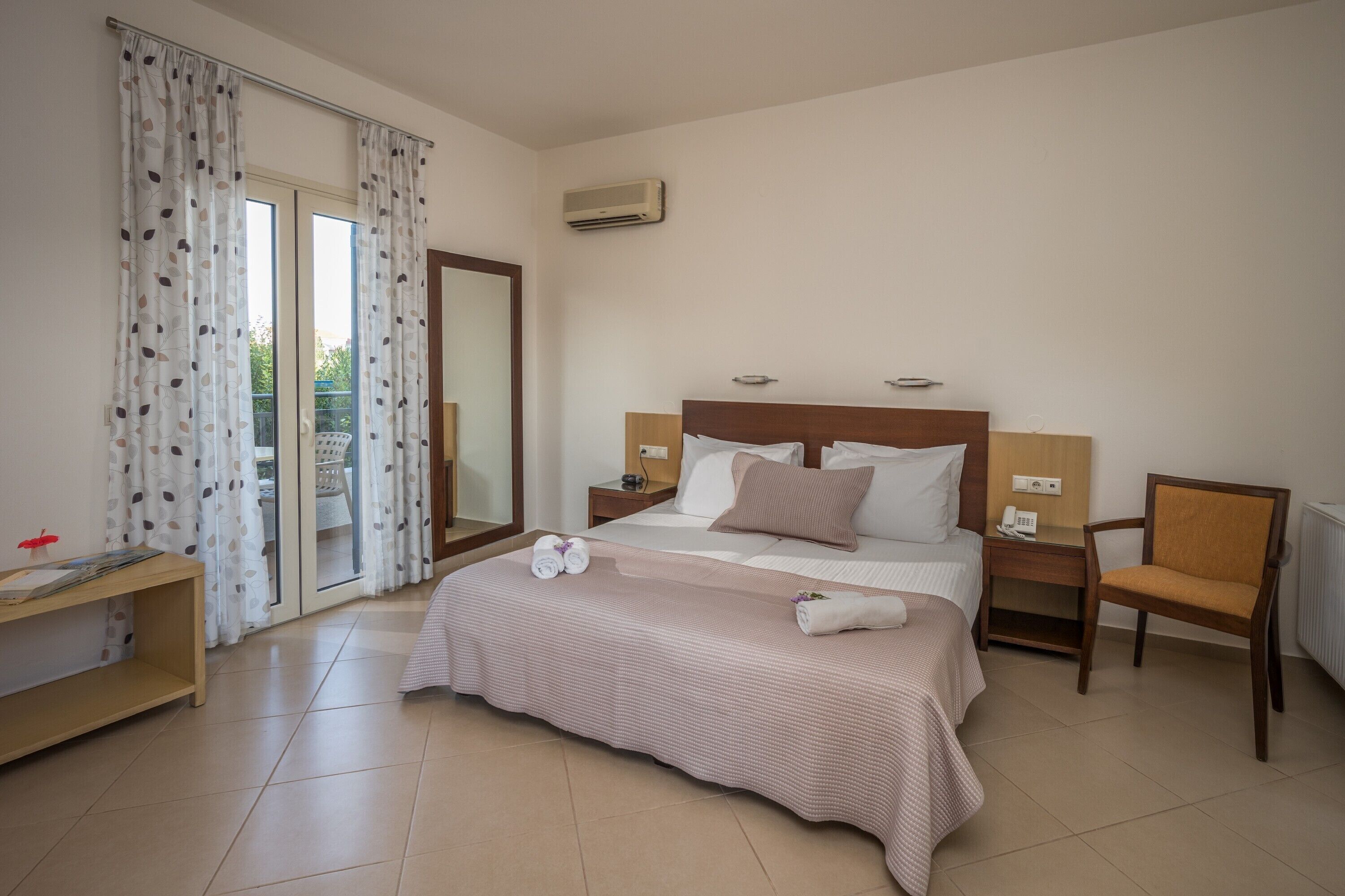 A hotel room with a large bed, a desk, a chair, and a sliding glass door to the balcony.