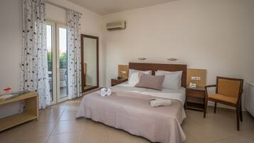A hotel room with a large bed, a desk, a chair, and a sliding glass door to the balcony.