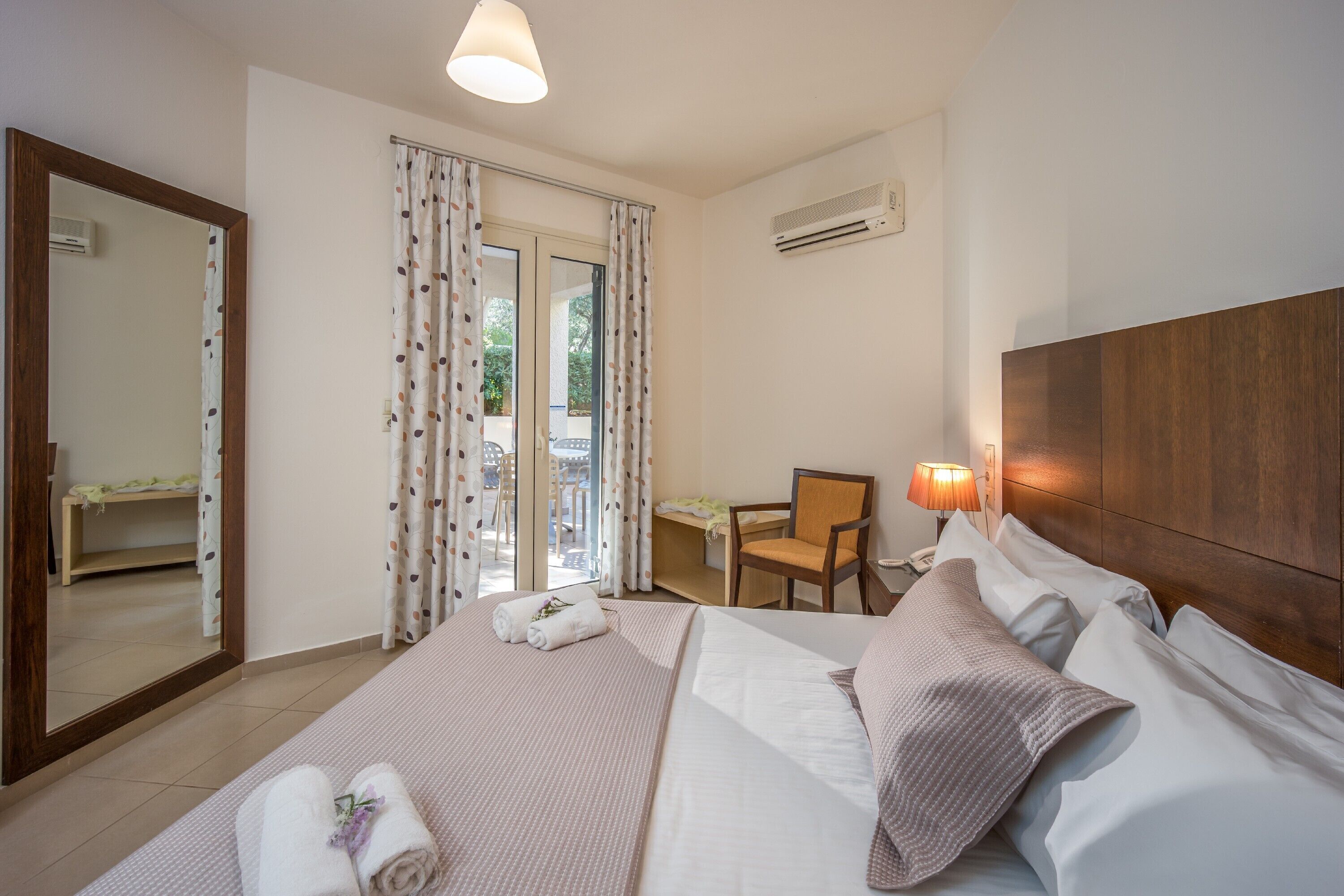 A hotel room with a large bed, a desk, a chair, and a view of the outdoors through a sliding door.