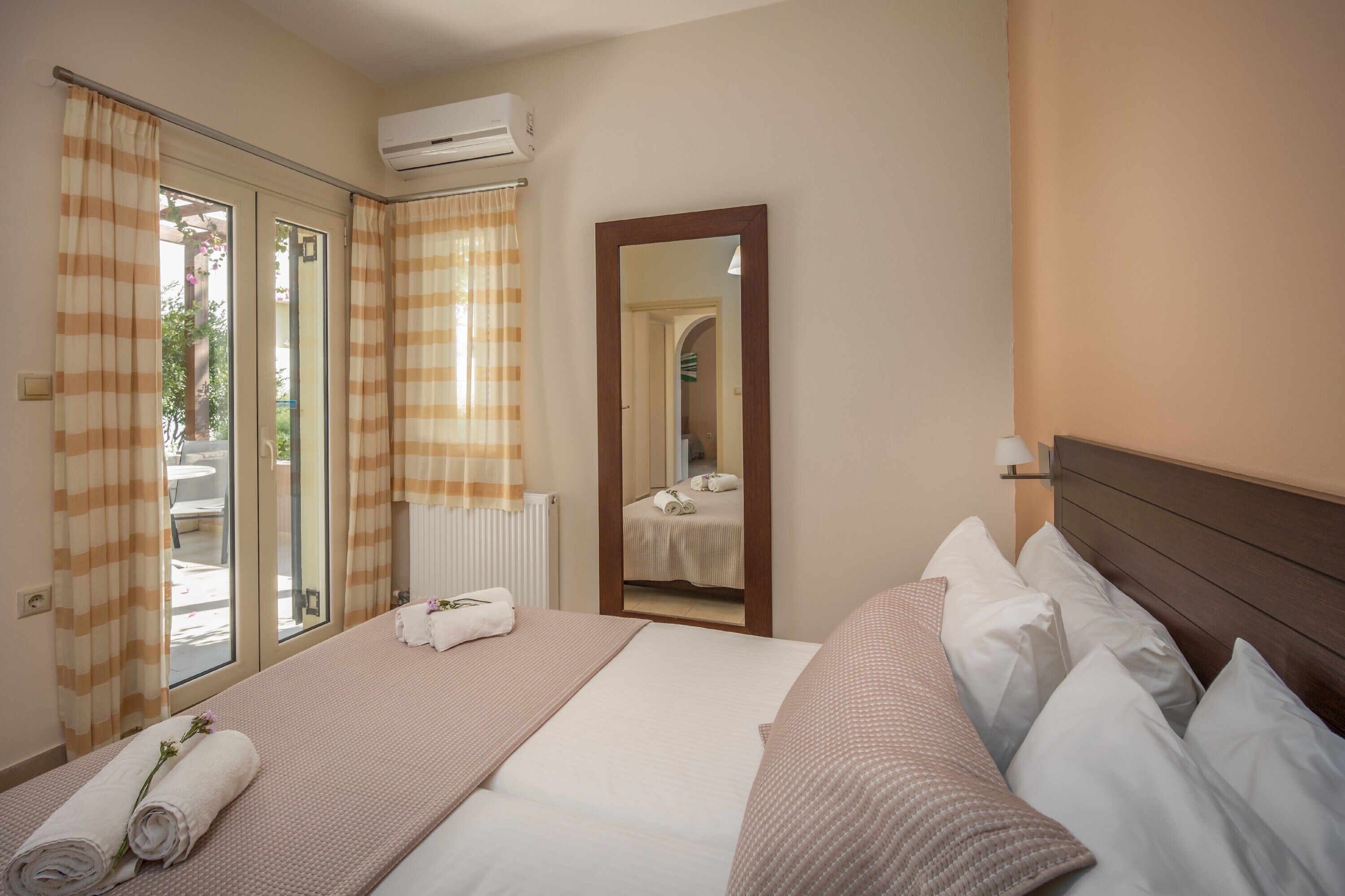 Una habitación de hotel con cama, ventana con cortinas, equipo de aire acondicionado y un espejo.