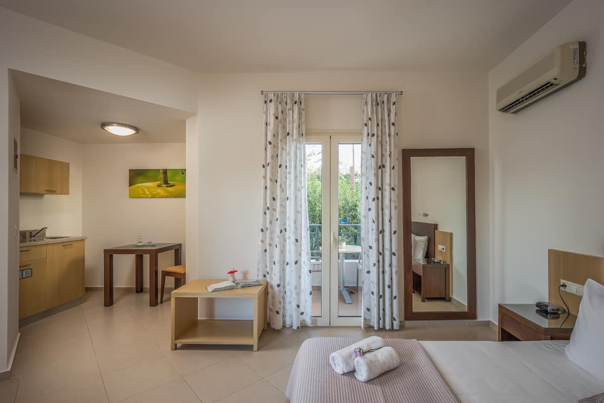 A hotel room with a bed, a desk, a chair, a small table, a mirror, and a view of the outdoors through a sliding door.