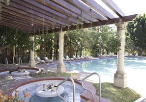 A pool area with a hot tub, lounge chairs, and a pergola with hanging plants. - Hotel Misión Comanjilla (Silao)