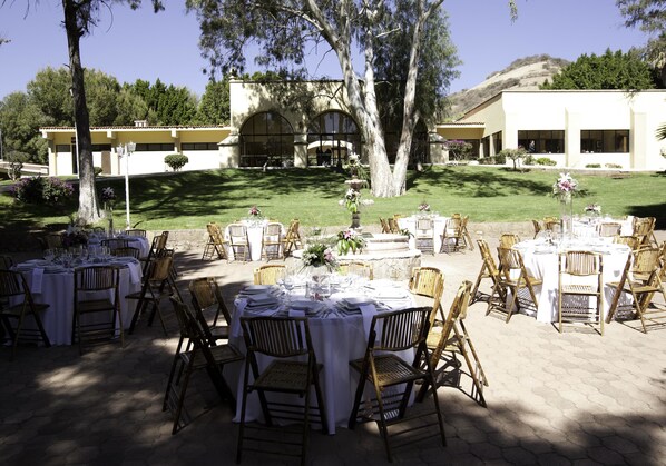 An outdoor dining area with round tables, wicker chairs, and white tablecloths. - Hotel Misión Comanjilla (Silao)