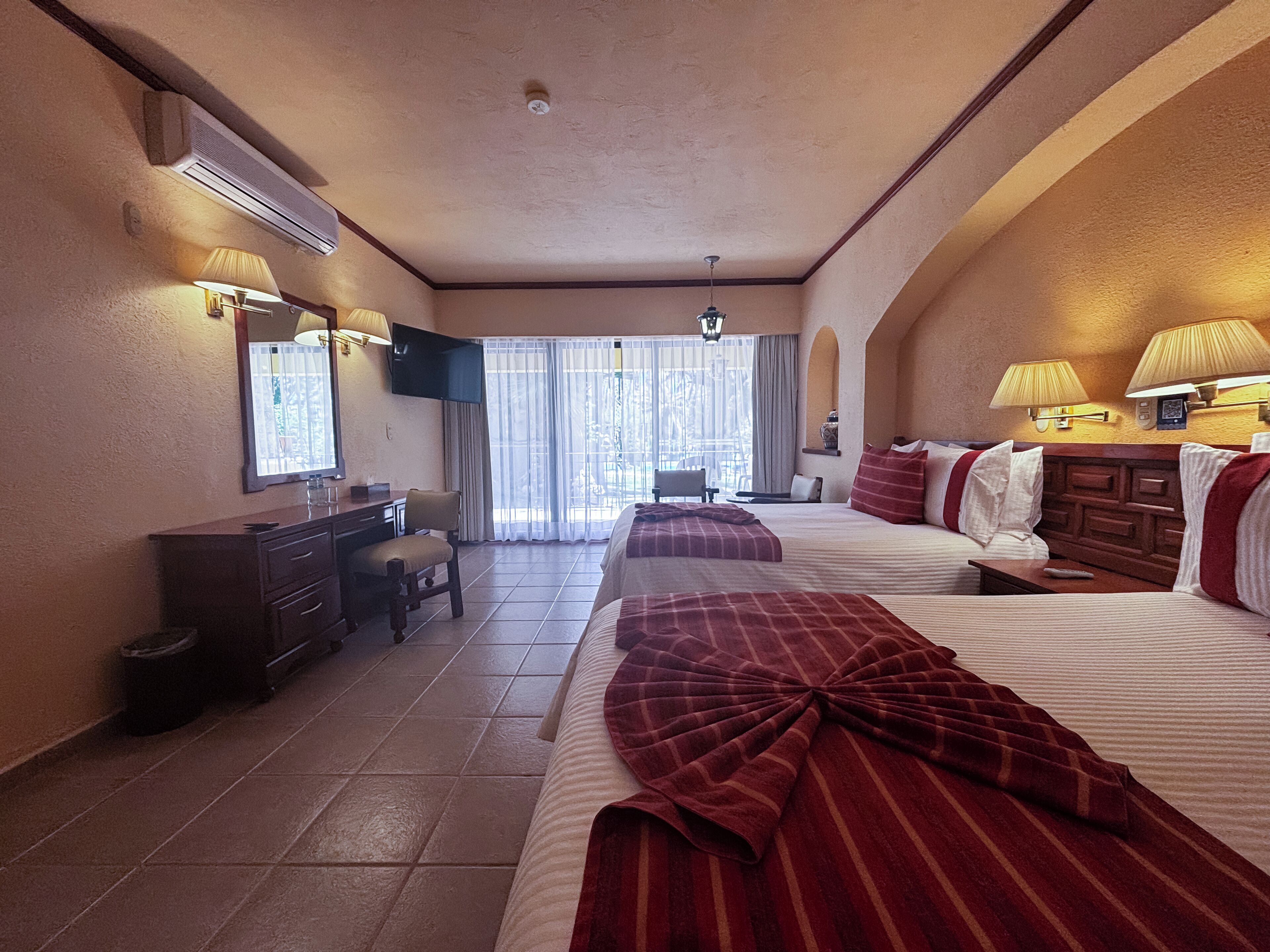 Habitación de hotel con dos camas, un escritorio, una silla, un televisor y una ventana con cortinas.