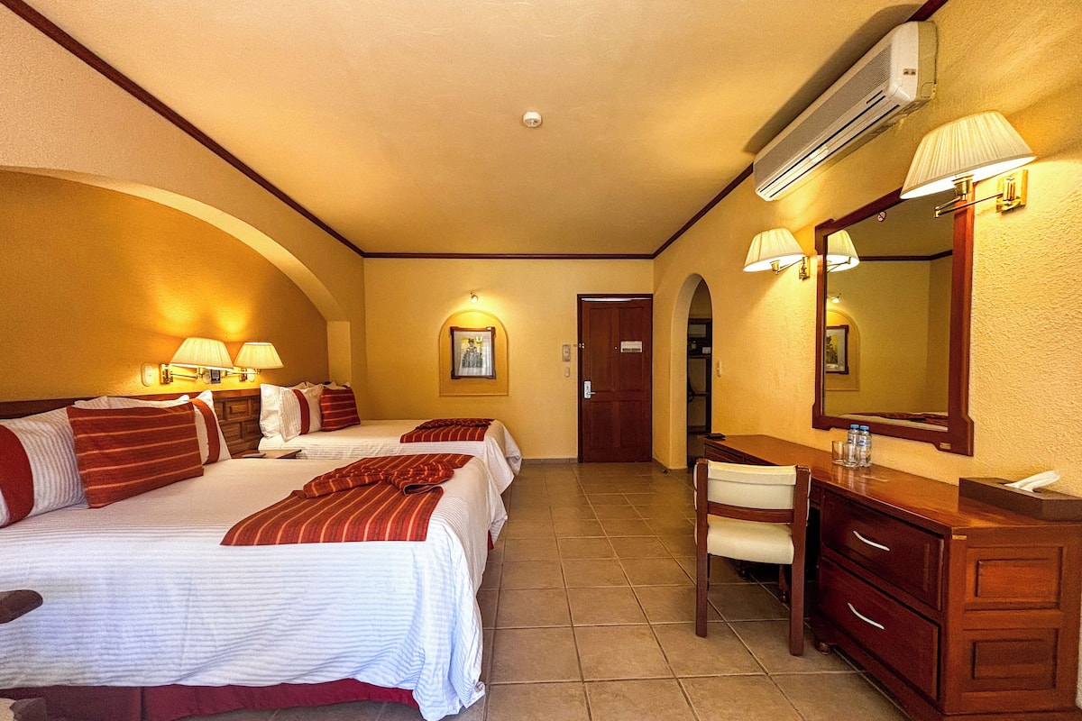 Ein Hotelzimmer mit zwei Betten, einem Schreibtisch, einem Stuhl, einem Spiegel und einer Badezimmertür.