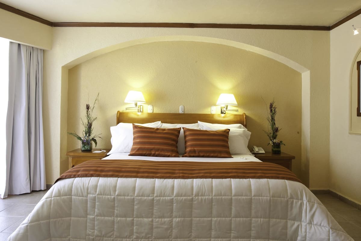Ein Hotelzimmer mit einem großen Bett, zwei Nachttischlampen, einem Holzkopfteil und einem kleinen Tisch mit einer Vase.