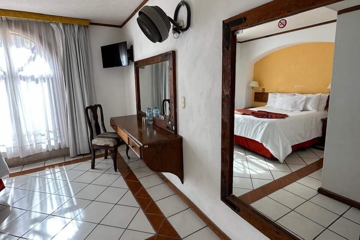 Ein Hotelzimmer mit Bett, Schreibtisch mit Spiegel, Stuhl, Fernseher und einem großen Spiegel, der das Bett reflektiert.