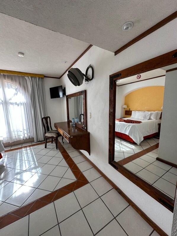 A hotel room with a bed, a desk with a mirror, a chair, a television, and a large mirror reflecting the bed. - Hotel Misión Comanjilla (Silao)