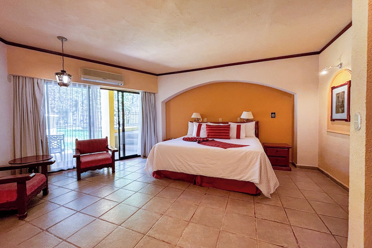 Ein Hotelzimmer mit Bett, Sessel, Tisch und Blick ins Freie.