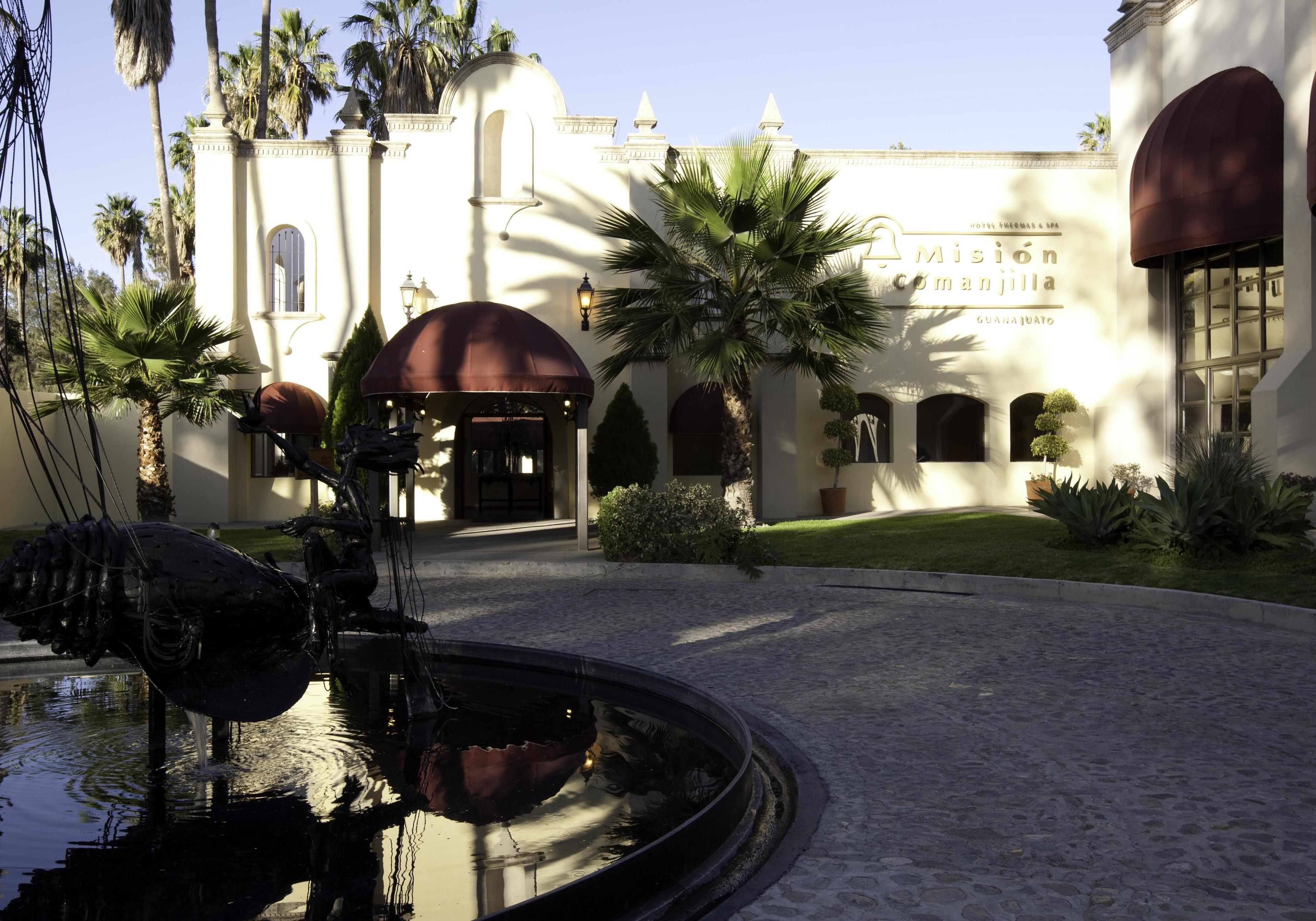 A hotel with a fountain, palm trees, and a white building with arches.