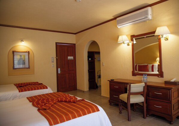 A hotel room with two beds, a desk, a chair, a mirror, and an air conditioning unit. - Hotel Misión Comanjilla (Silao)