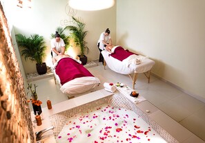 A spa room with two massage tables, a bathtub with rose petals, and potted plants. - Hotel Misión Comanjilla (Silao)