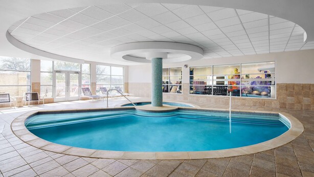 An indoor swimming pool with a curved design, a central pillar, and a ceiling with a grid pattern. - Hilton Garden Inn Dallas Richardson (Richardson)