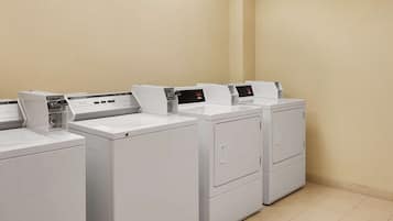 A row of white front-loading washers in a laundry room with beige walls and tiled flooring.