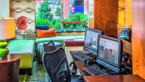 A compact hotel room with a desk, computer, and seating area.