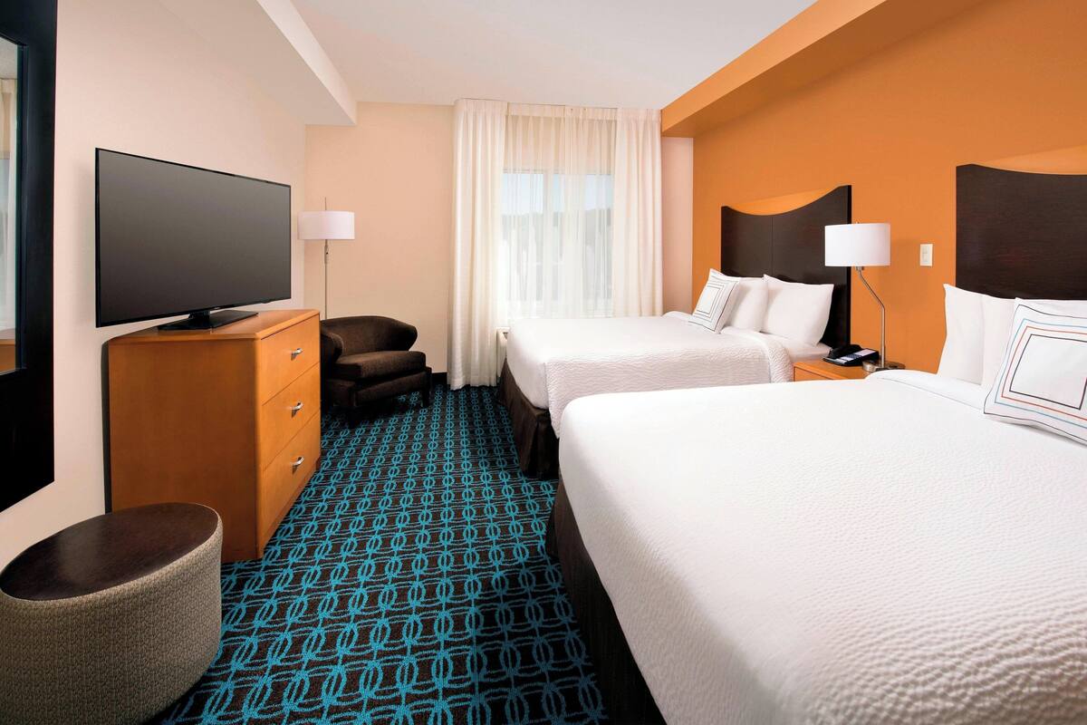 A hotel room with two beds, a television, a desk, and a chair.